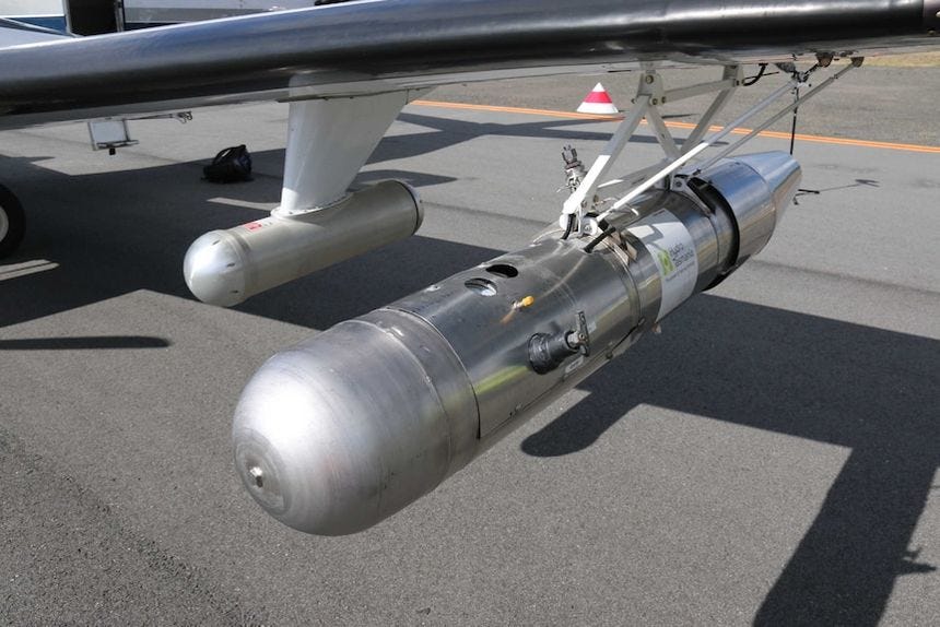A silver canister hanging from the wing of a plane. A silver canister hanging from the wing of a plane.