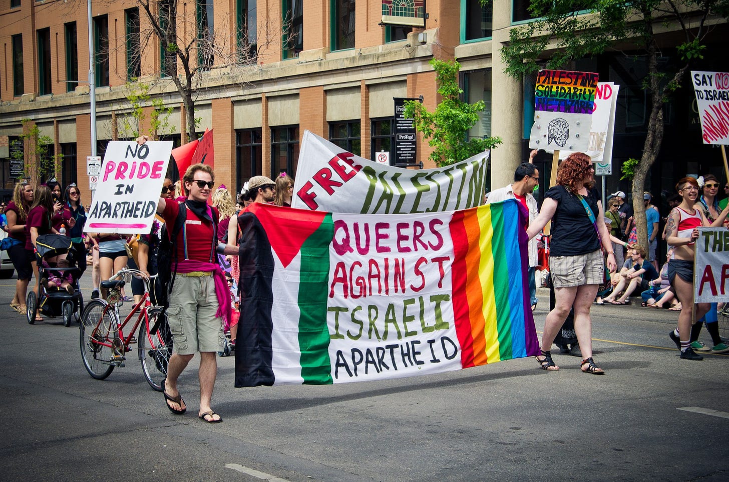 people marching holding signs that say "no pride in apartheid" "free palestine" and "queers against israeli apartheid" people marching holding signs that say "no pride in apartheid" "free palestine" and "queers against israeli apartheid"