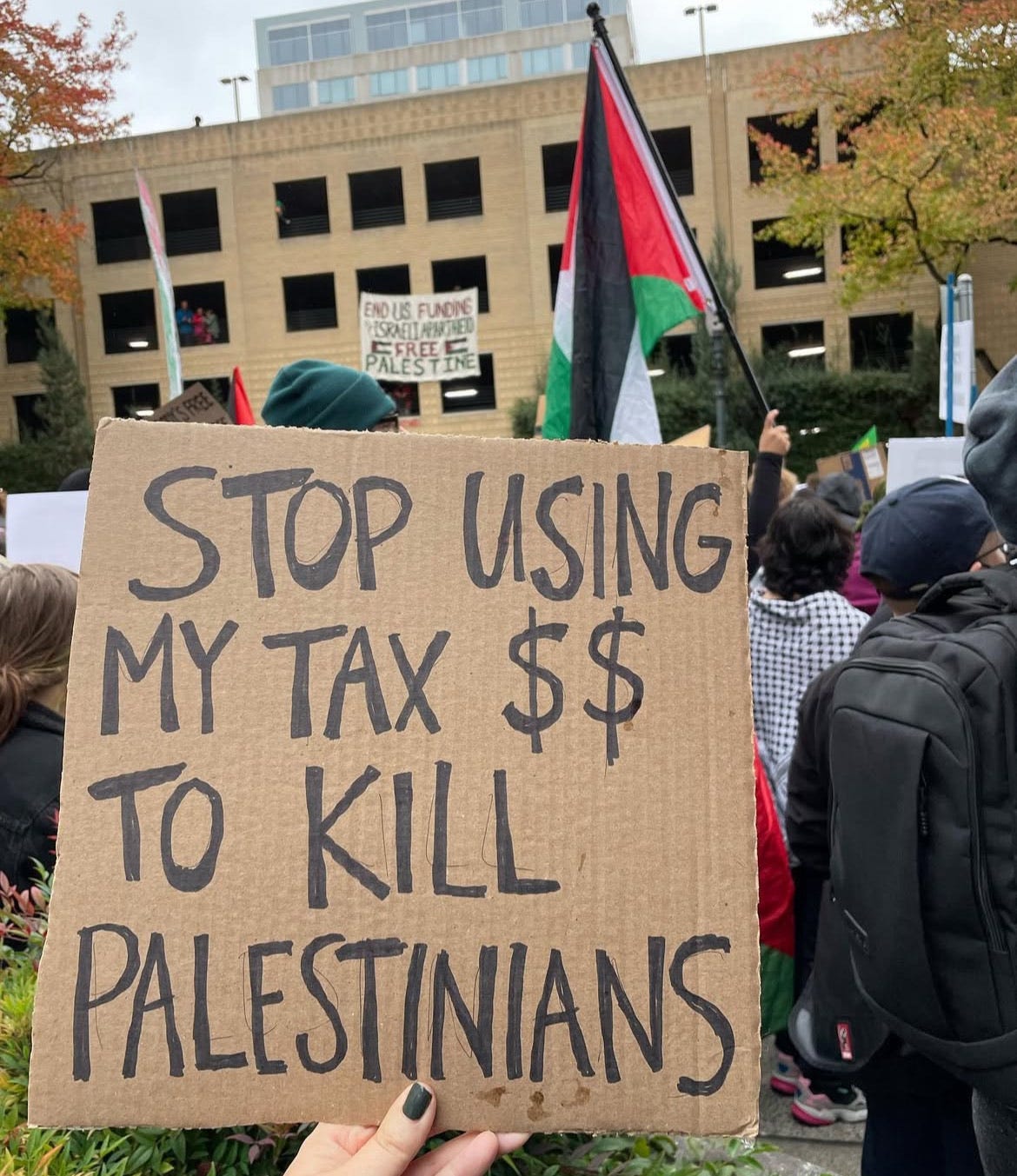 a cardboard sign in front of a building in downtown portland says stop using my tax dollars to kill palestinians
