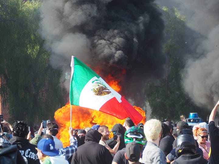 Protesters gathering around three burning and vandalized Waymo rideshare vehicles in Downtown Los Angeles.