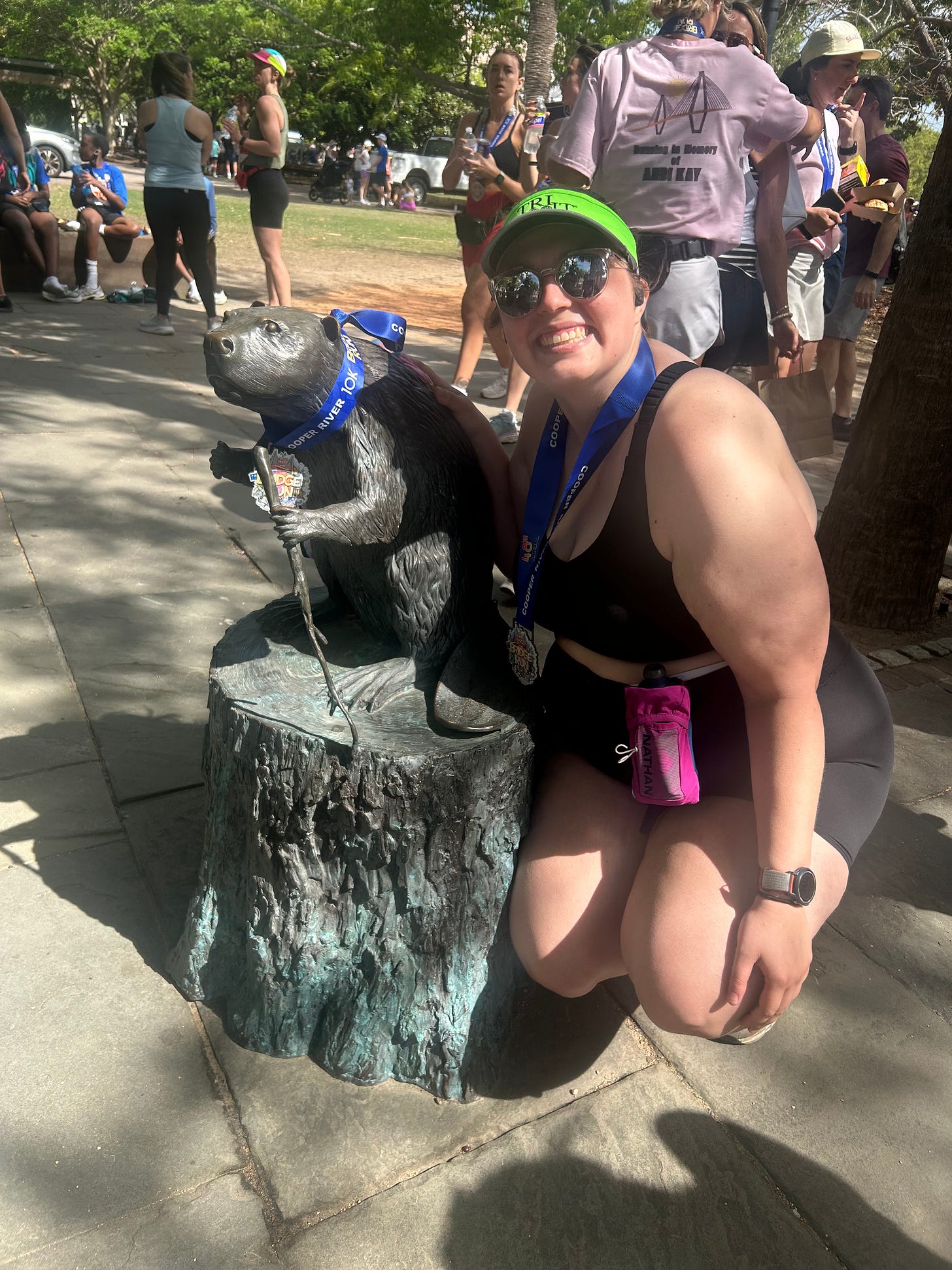 Sydney squats next to a statue of a beaver. She and the beaver both wear medials for the 2025 bridge run. 
