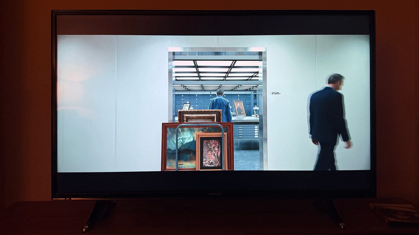 A picture of a TV with Severance playing; a white corridor leading to a studio, in the foreground paintings on a trolley A picture of a TV with Severance playing; a white corridor leading to a studio, in the foreground paintings on a trolley