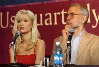 A blond woman next to a bearded middle-aged man with glasses, both sitting at a table with microphones. A blond woman next to a bearded middle-aged man with glasses, both sitting at a table with microphones.