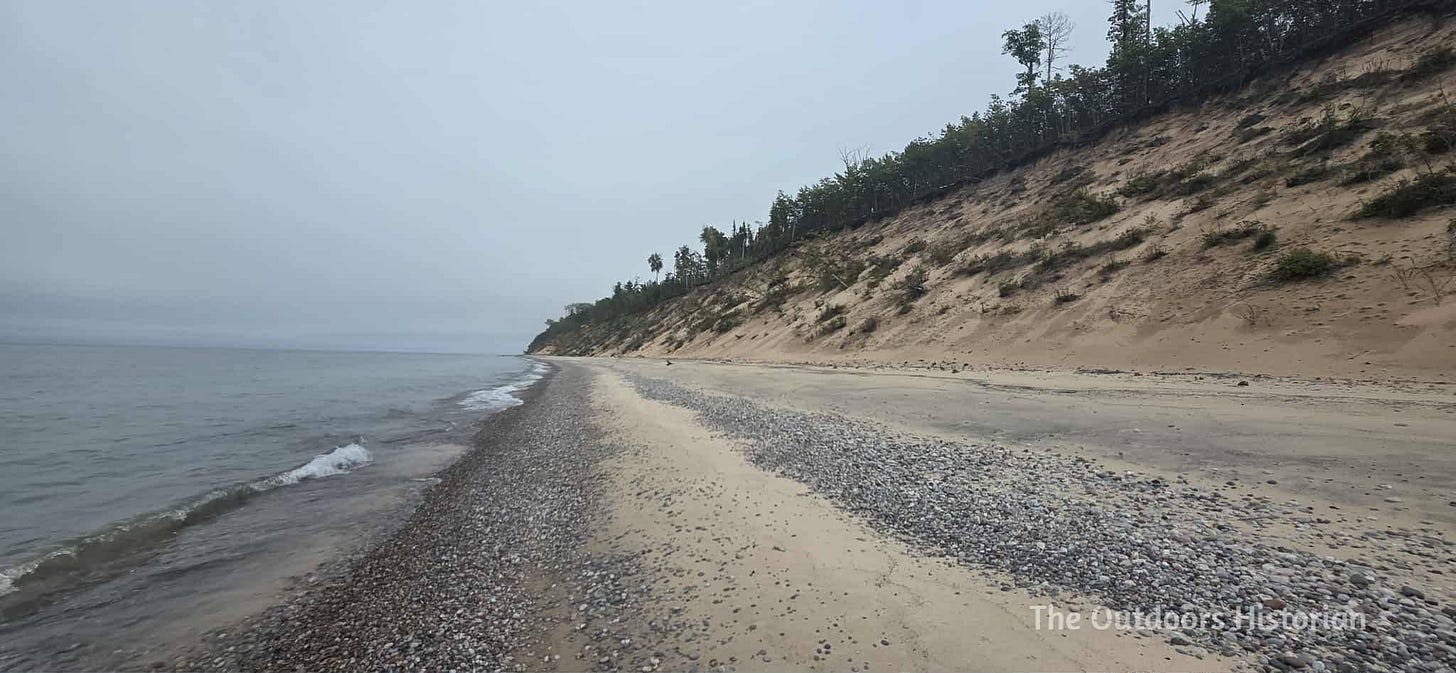 A sandy beach with many small rocks along the waterline and a steep dune stretching off into the horizon.
