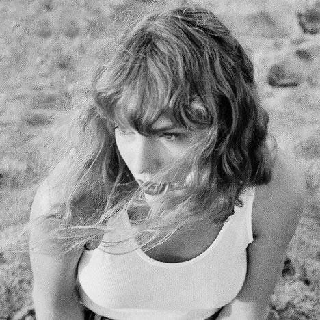 This may contain: black and white photograph of a woman sitting on the ground with her hair blowing in the wind