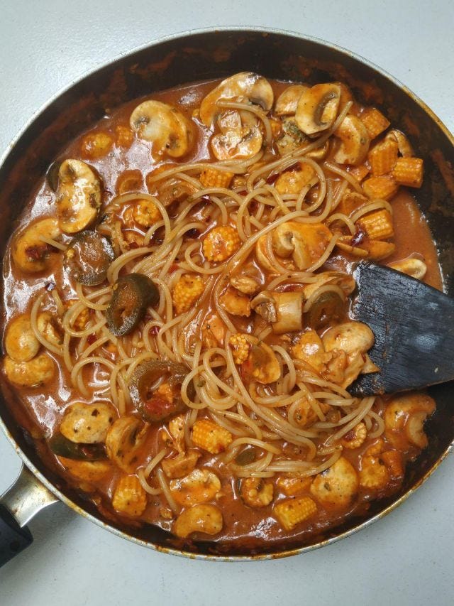 A pan of noodles in red sauce with mushrooms, baby corn and jalepenos. A pan of noodles in red sauce with mushrooms, baby corn and jalepenos.