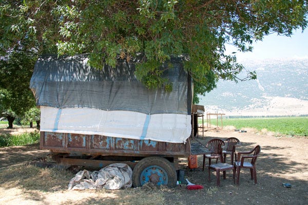 A covered wagon is parked in the countryside. There are 4 brown palstic chairs in front of it. A covered wagon is parked in the countryside. There are 4 brown palstic chairs in front of it.