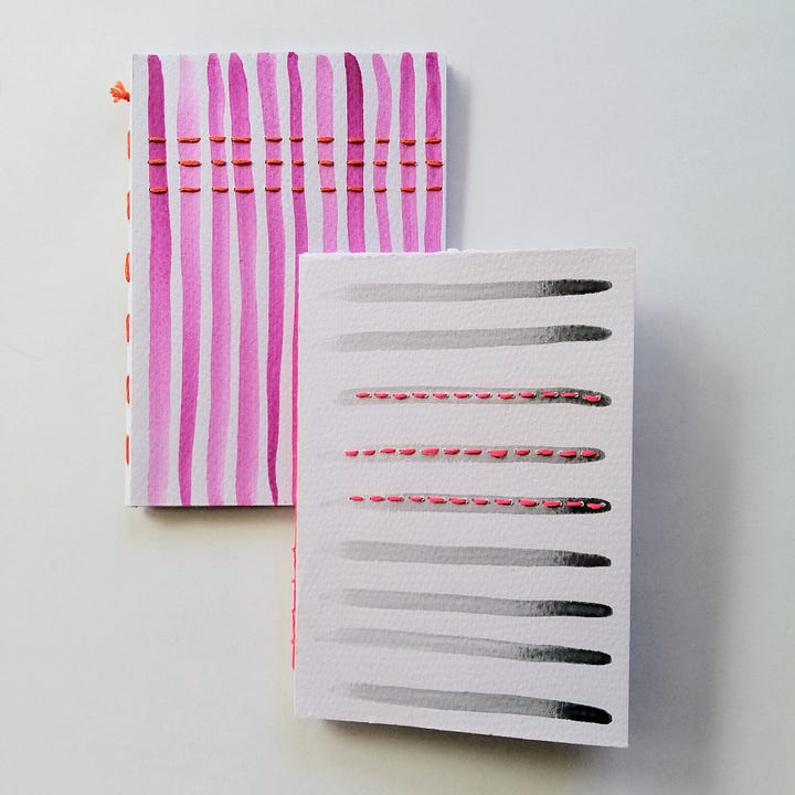 Four watercolour painted handmade notebooks with stitched details.
