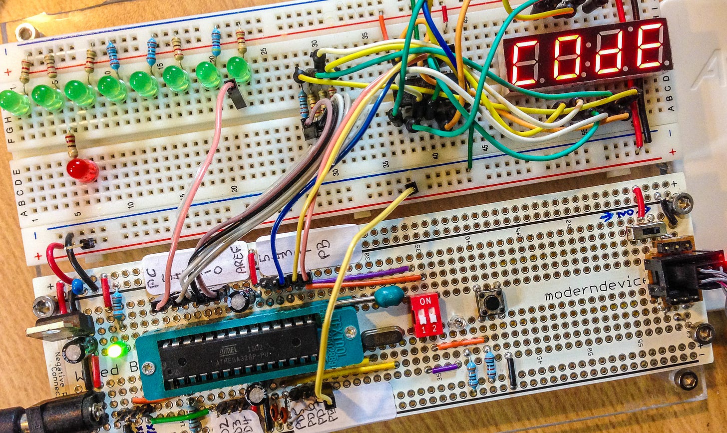 Close-up photograph of an electronics prototyping breadboard with chips, many wires and a display that says 'Code'