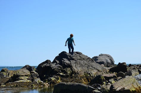 Lighthouse in Maine with rocky beaches and children playing.