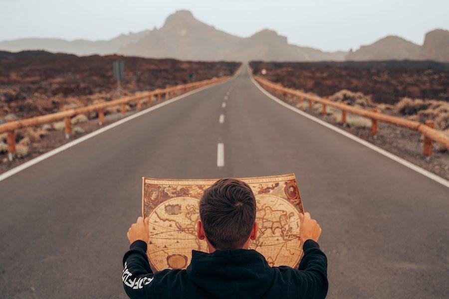 Man reviewing map facing road and mountains Man reviewing map facing road and mountains