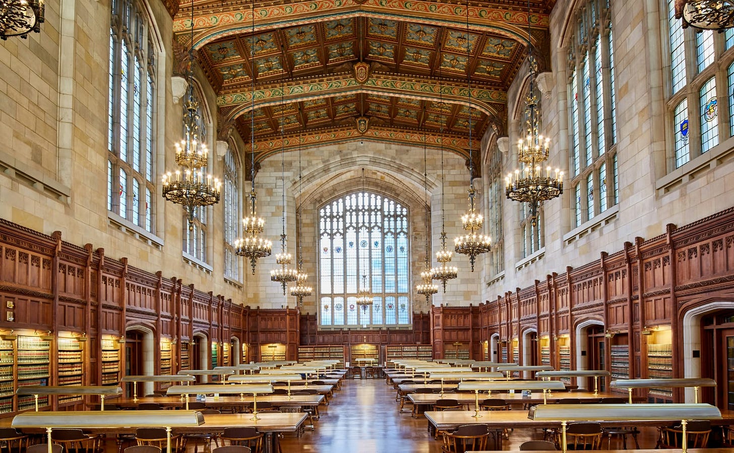 large reading room with rows of tables under a vaulted ceiling with gothic chandeliers and stained glass windows