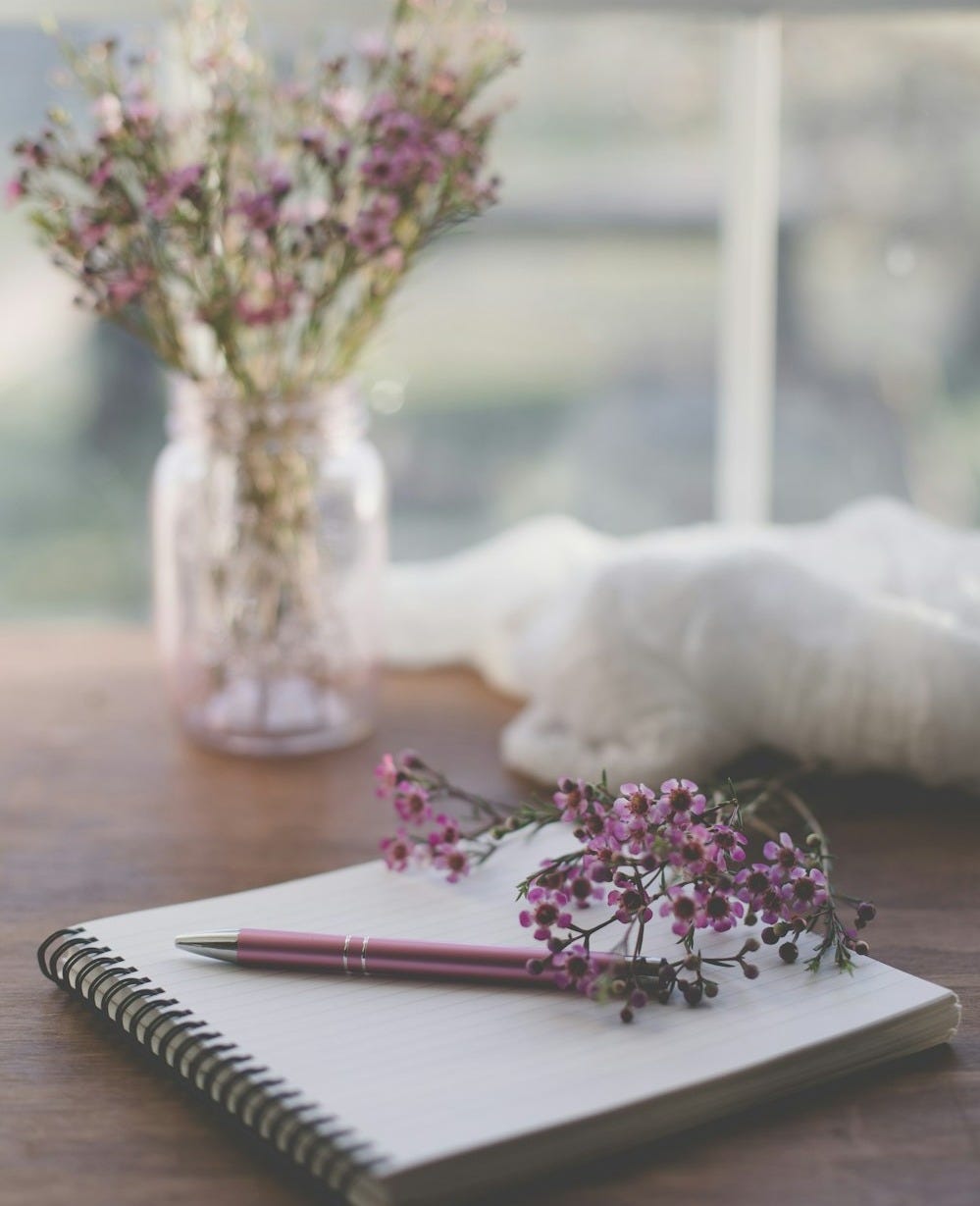 shallow focus photo of purple flowers on white spiral notebook shallow focus photo of purple flowers on white spiral notebook