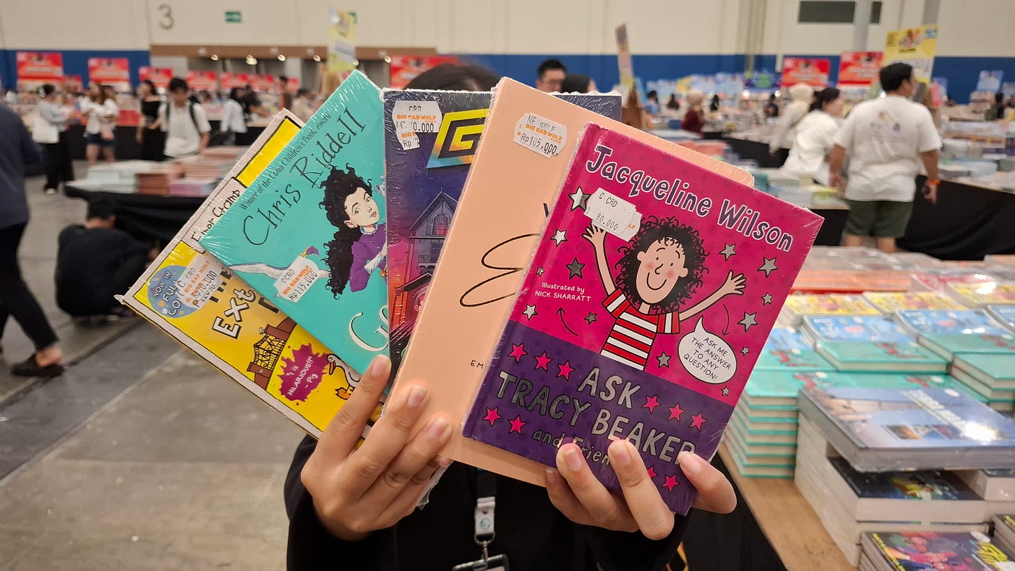A jastiper (personal shopper providing a jastip or personal shopping service) sorting, selecting, and packing books at a large book fair, organizing customer orders from multiple requests for delivery after purchase.