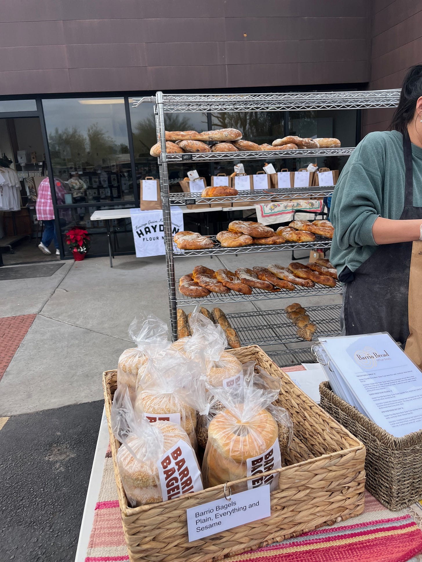 A picture of the table where I buy the bread, with shelves of bread in the background outside of the Hayden flour mills warehouse