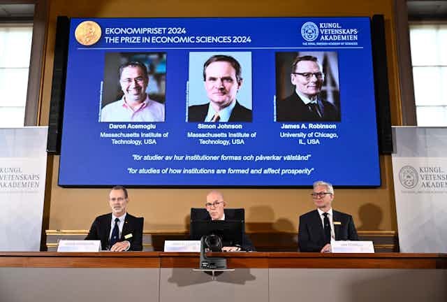 Three men in suits announcing the winners of the 2024 Nobel prize in economics. Three men in suits announcing the winners of the 2024 Nobel prize in economics.
