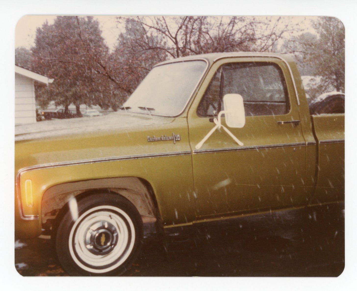green chevy truck taken so only the front end is visible; snow is falling