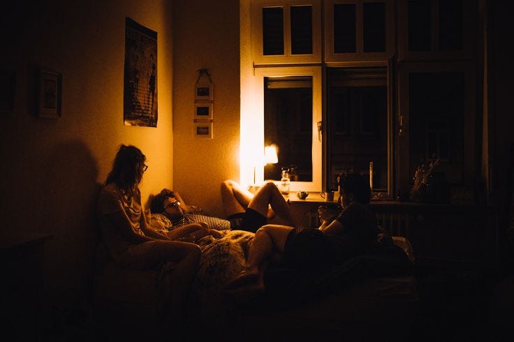 This may contain: two people sitting on a couch in a dark room, one person is reading the book
