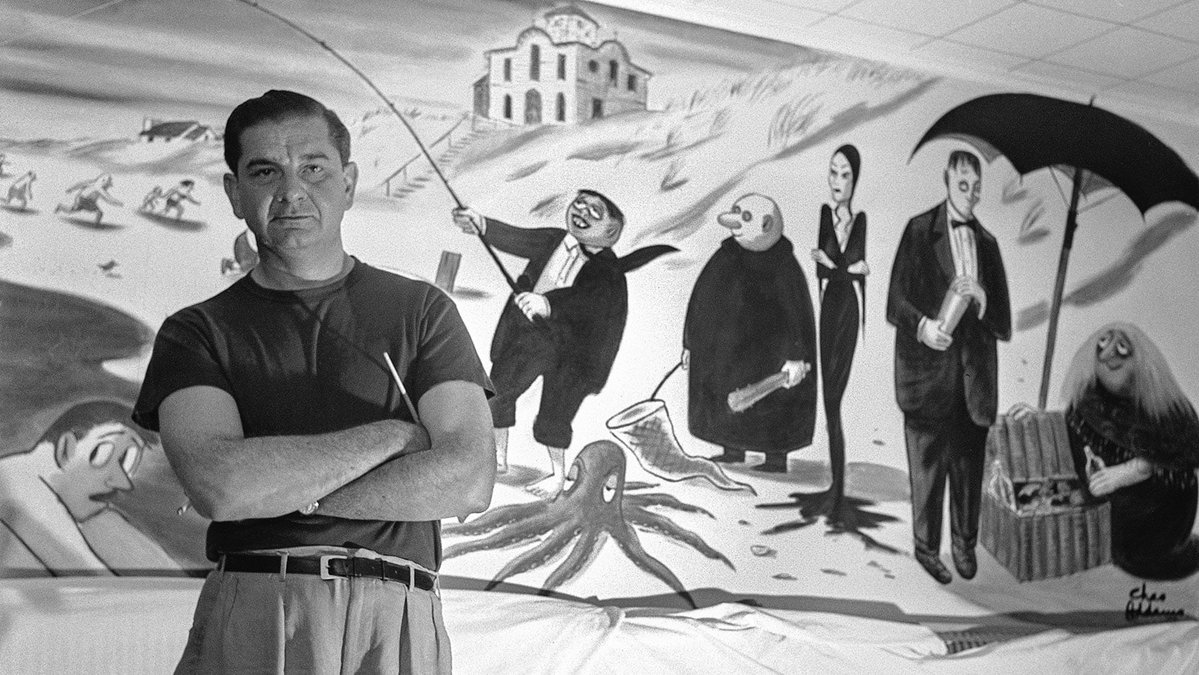 Charles Addams poses with a cartoon of the Family