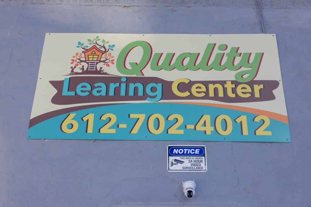 Quality Learning Center sign on a light blue wall, with a surveillance camera and "Notice: This Area is Under 24 Hour Video Surveillance" sign below.
