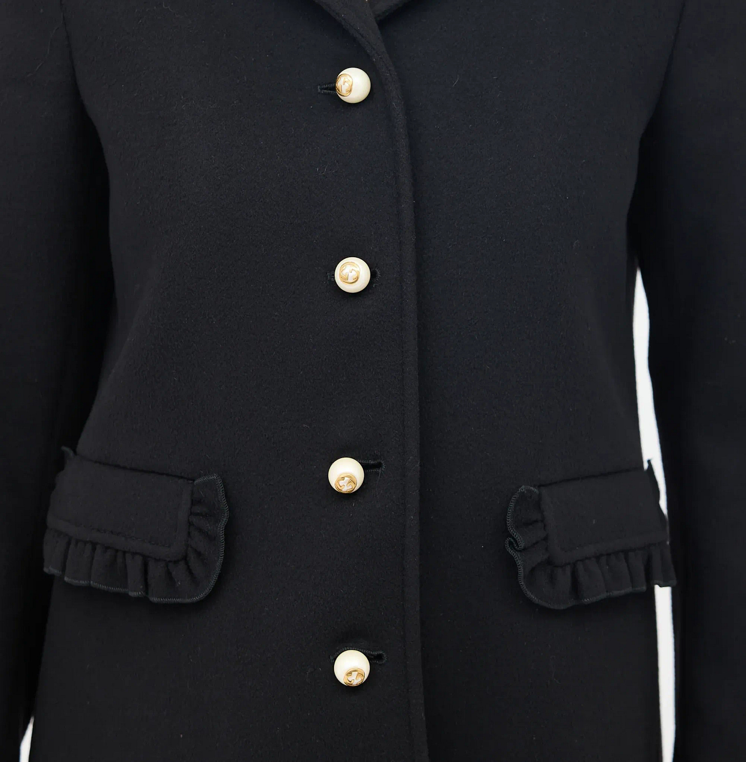 Close-up of a black wool coat with pearl buttons and ruffled pocket details
