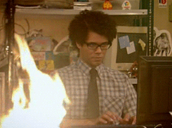 Gif de IT Crowd con uno de los protagonistas con camisa de manga corta de cuadros con una corbata y fuego a su alrededor
