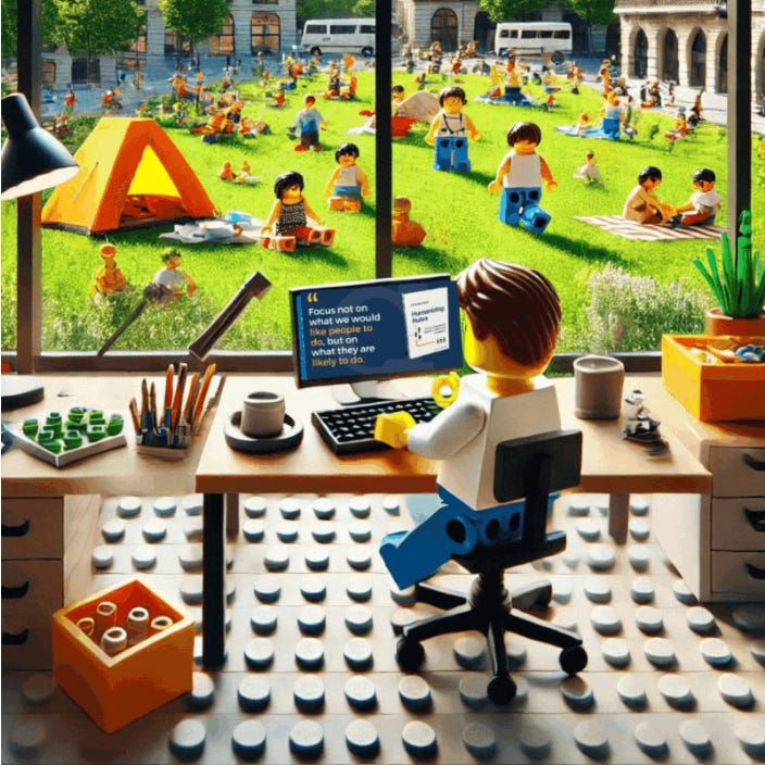 Lego minifigure working at a computer inside a modern office with a large window. Outside, a park scene shows numerous Lego people relaxing, playing, and enjoying a sunny day. A quote on the screen reads: "Focus not on what you would like people to do, but on what they are likely to do."