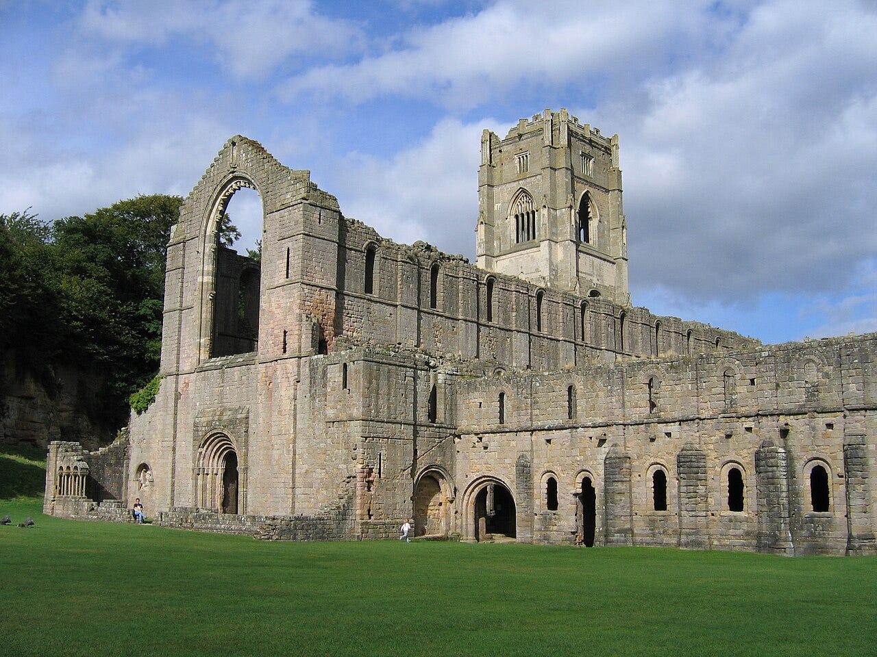 The ruined church and tower of Fountains Abbey seen across open grass.