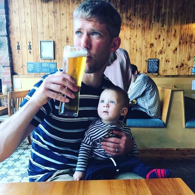 Andy Carter holding a baby while drinking a pint in a pub.