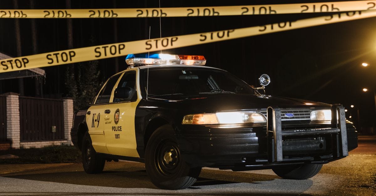 Photo: cottonbro studio / Pexels A police car parked at a night crime scene with yellow barricade tape, under streetlights.