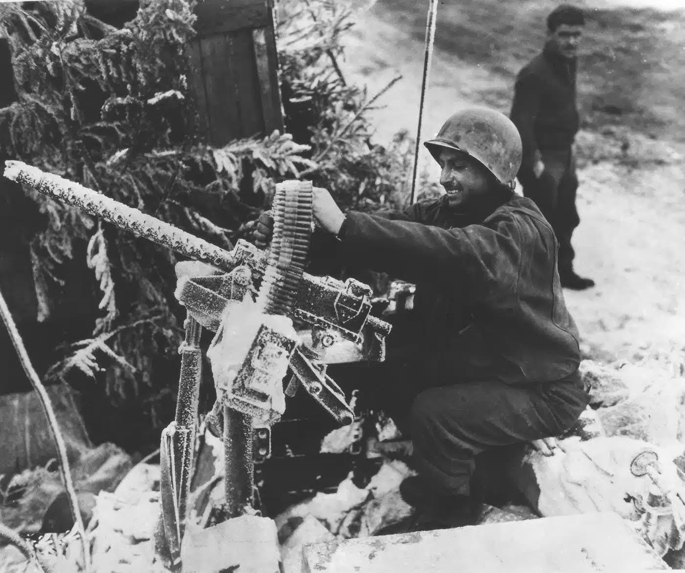 A GI from the 5th Armored Division prepares a frost-covered Browning M1919A4 machine gun in Belgium, January 1945, amidst the harsh winter of WWII.