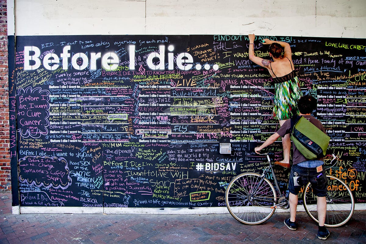 Members of the public write personal hopes and aspirations in chalk on Candy Chang's interactive “Before I Die…” wall.