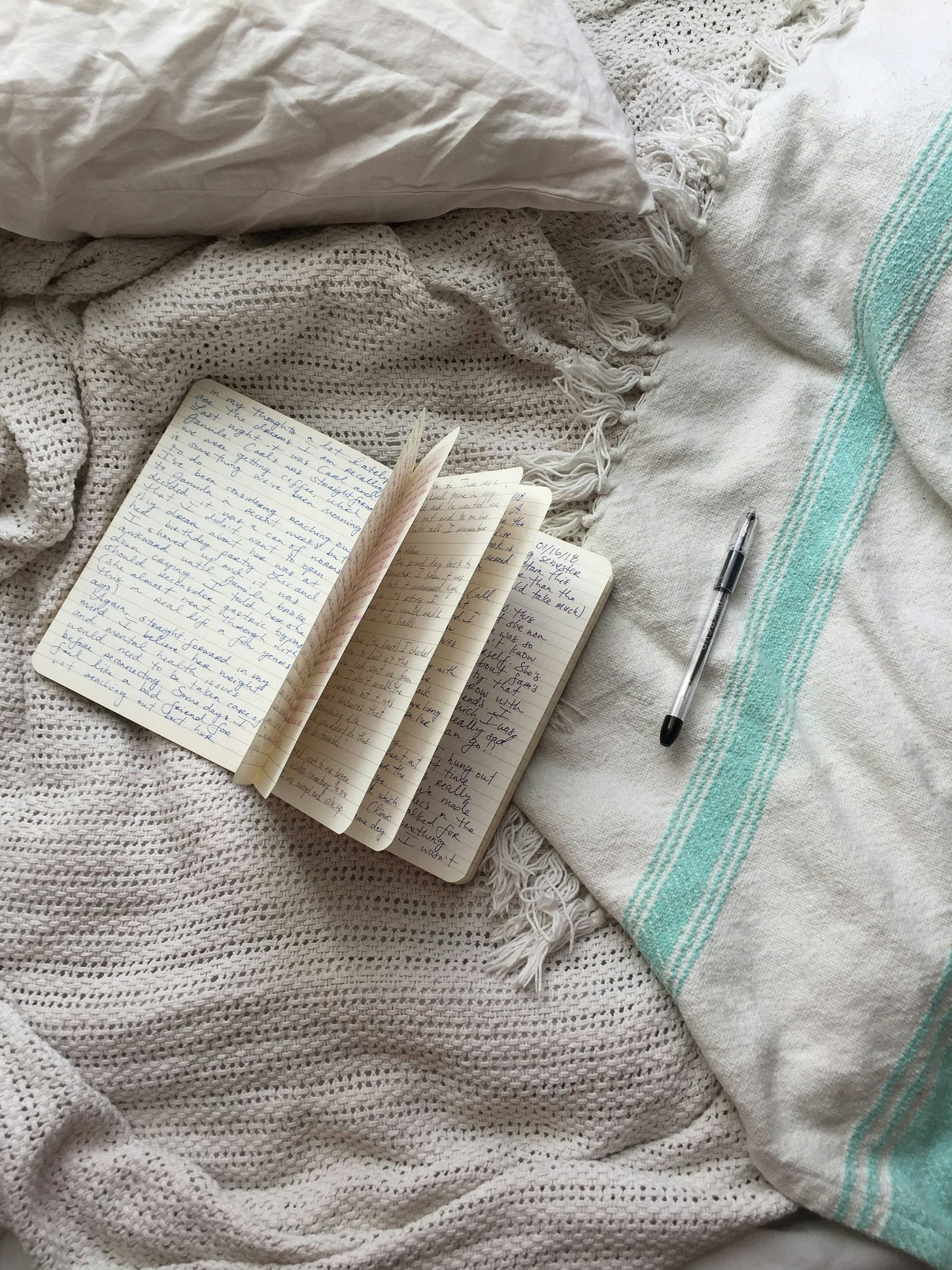 A notebook filled with writing lying open next to a pen on a bed with blankets A notebook filled with writing lying open next to a pen on a bed with blankets
