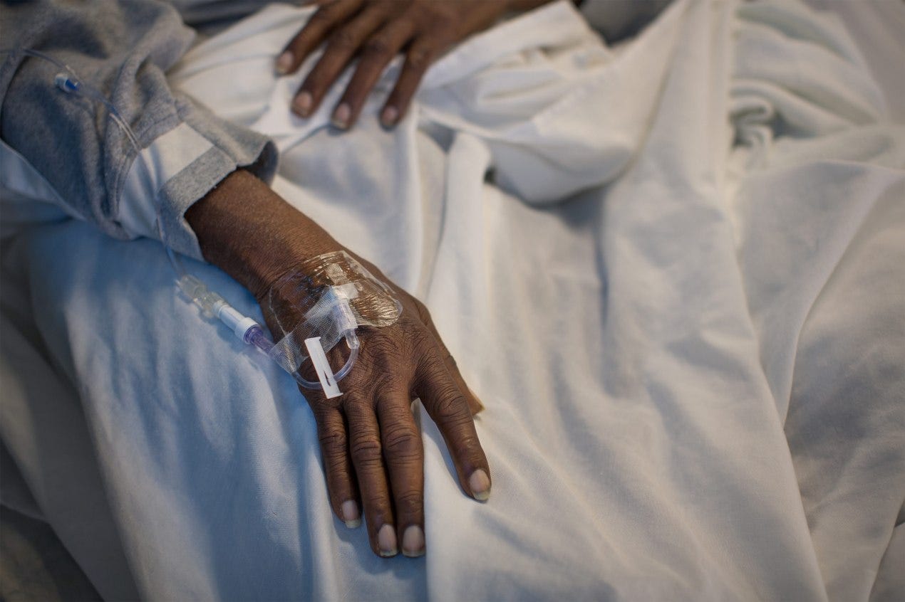 A photo of a black man's hand with an IV in the top of his hand. A photo of a black man's hand with an IV in the top of his hand.