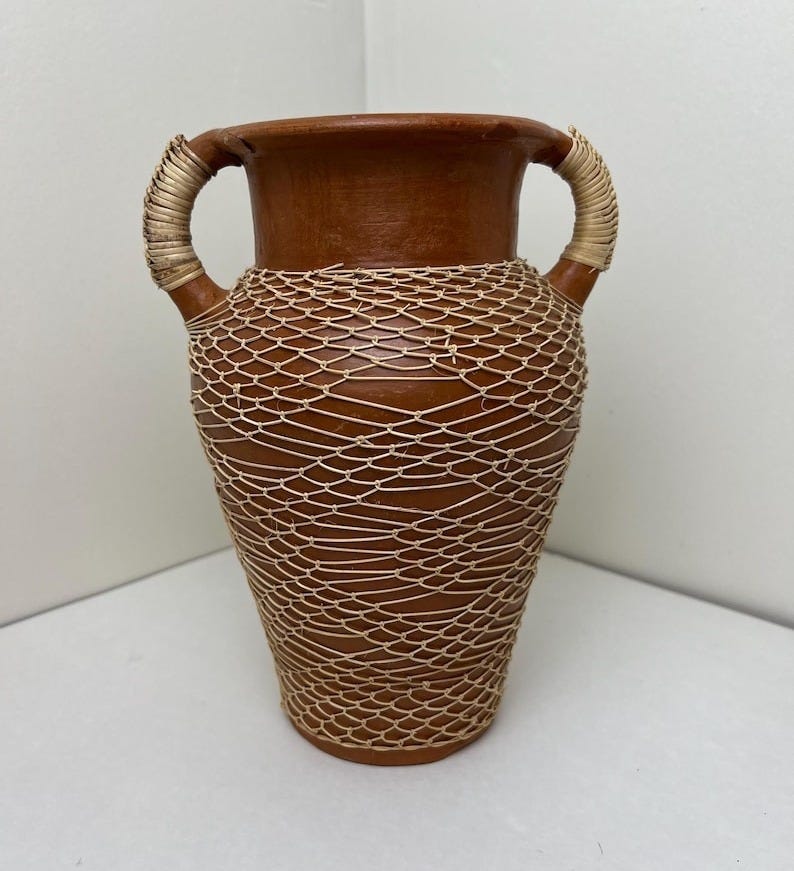 May include: A brown ceramic vase with a woven straw design. The vase has two handles and a rounded body.