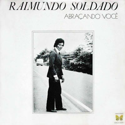 Capa do disco Abraçando Você, de Raimundo Soldado. No centro, uma foto de Raimundo tirada nos anos 80. Ele é um homem negro, de paletó e calças largas, posando para a foto na beira de uma estrada. Capa do disco Abraçando Você, de Raimundo Soldado. No centro, uma foto de Raimundo tirada nos anos 80. Ele é um homem negro, de paletó e calças largas, posando para a foto na beira de uma estrada.