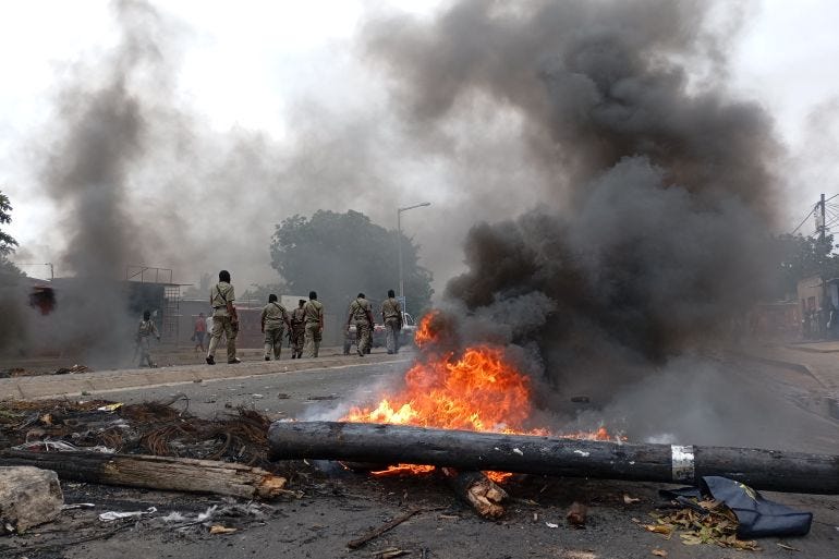 Pedestrians walk past a burning barricade in Maputo on December 24, 2024. - The capital of Mozambique was deserted on Tuesday, its main arteries heavily secured, noted AFP, the day after the confirmation of the victory in the October elections of Frelimo, in power for half a century, while the opposition maintains his denunciations of fraud. Maputo remains frozen in a climate of fear and insecurity on Christmas Eve after violent demonstrations in the evening and night. The police, in armored vehicles, patrol the center. (Photo by Amilton Neves / AFP)