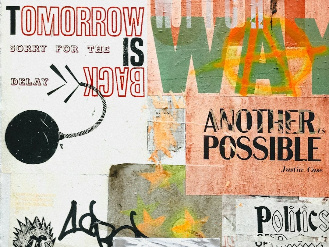 man in blue denim jeans and black jacket standing beside wall with graffiti