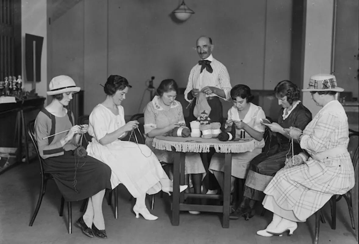 old photo of women knitting while a man stands in the middle of them