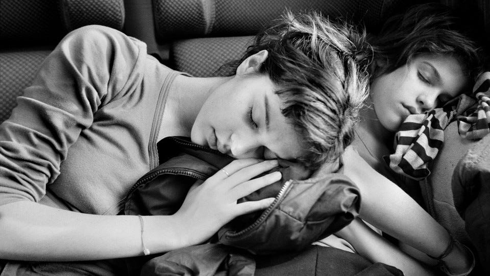 a black and white photo of two girls asleep while sitting, one leaning on the other