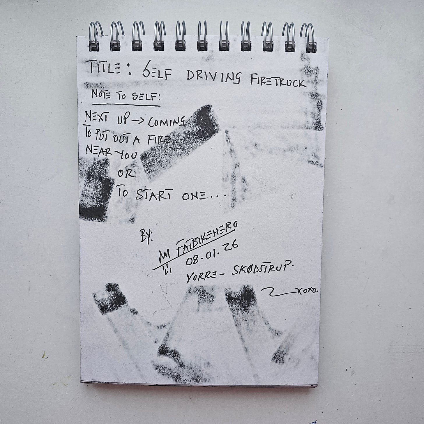"The back of a sketchbook page with handwritten text in black ink. The text reads: 'Title: SELF DRIVING FIRETRUCK. Note to Self: Next up -> Coming to put out a fire near you OR To start one...' The page is signed 'M FatbikeHero', dated '08.01.26', and inscribed 'Vorre - Skødstrup'. Heavy black marker ink from the front image has bled through the paper, creating a textured, shadowy pattern of the truck's shape on the reverse."