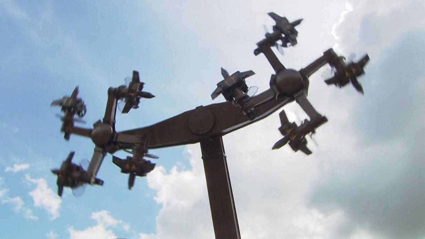 A fairground ride in motion. Four cabins for passengers extend from a central point at right angles, forming a swastika.