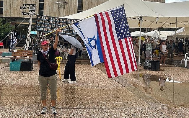 Miki Ziv waves US and Israeli flags in Tel Aviv's Hostages Square on October 9, 2025. (Ben Sales/Times of Israel)