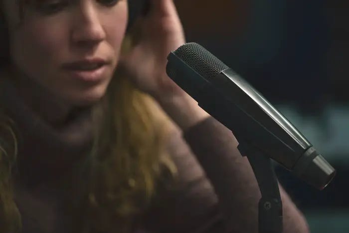 Microfone em destaque e mulher ao fundo com as maos no ouvido