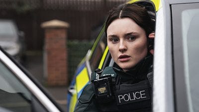 A woman in police uniform leans out the door of a police car looking concerned A woman in police uniform leans out the door of a police car looking concerned