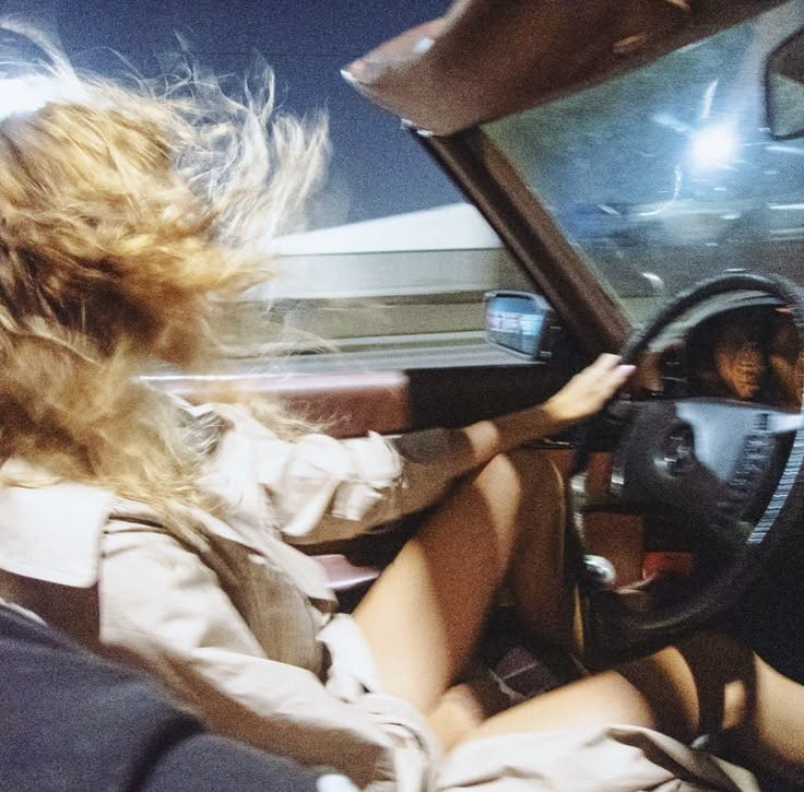 This may contain: two women sitting in the driver's seat of a car, one with her head on the steering wheel