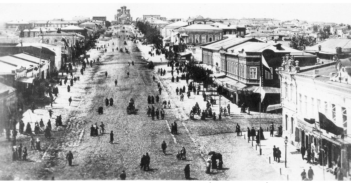 Old black and white photo of a very wide street taken from above with people walking on and off the street. The photo is taken from above and there is a large orthodox church at the end of the center of the street.