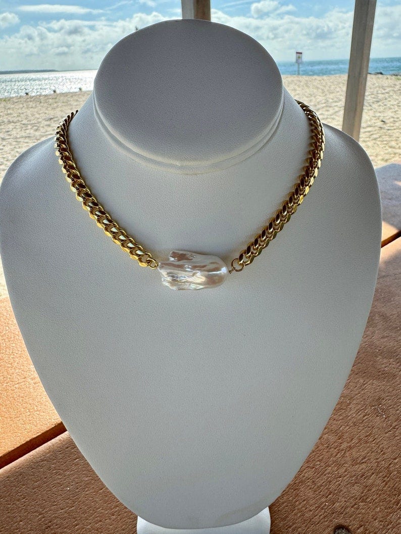 May include: A gold chain necklace with a large white pearl pendant.