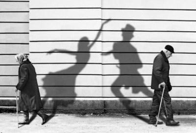 This may contain: two people are walking down the street with their shadows on the wall and one is holding a cane