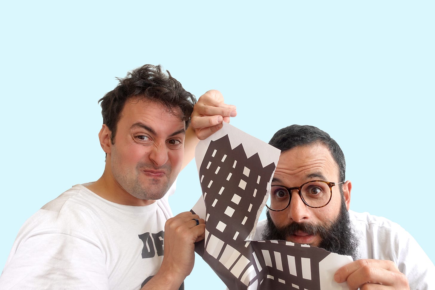Two middle-aged men with brown hair hold a picture of a building and are tearing it up while looking in the camera. Two middle-aged men with brown hair hold a picture of a building and are tearing it up while looking in the camera.